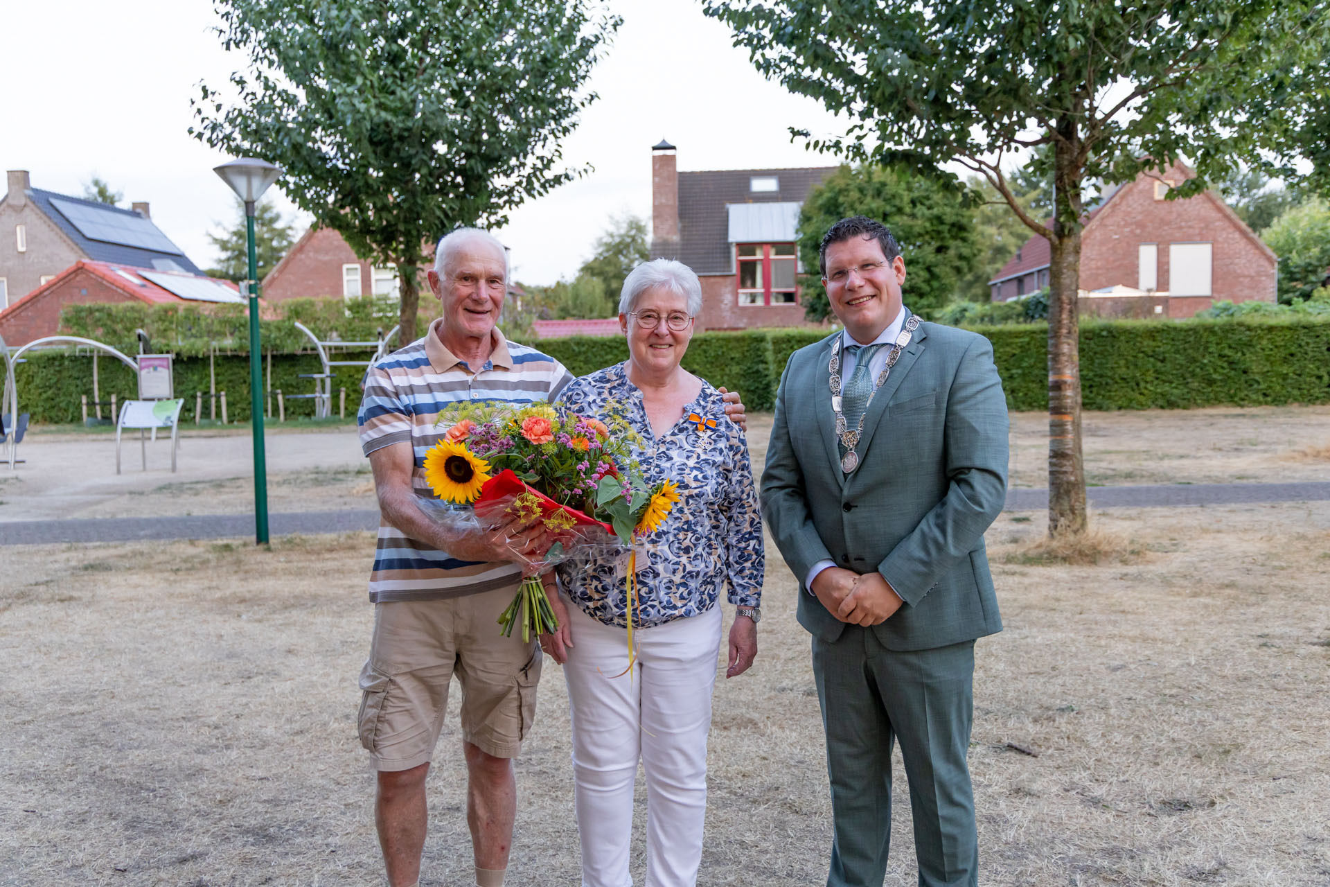 José De Kleijnen-van Kempen en haar man Jan met locoburgemeester Mark Janssen en een bos bloemen bij een speeltuintje